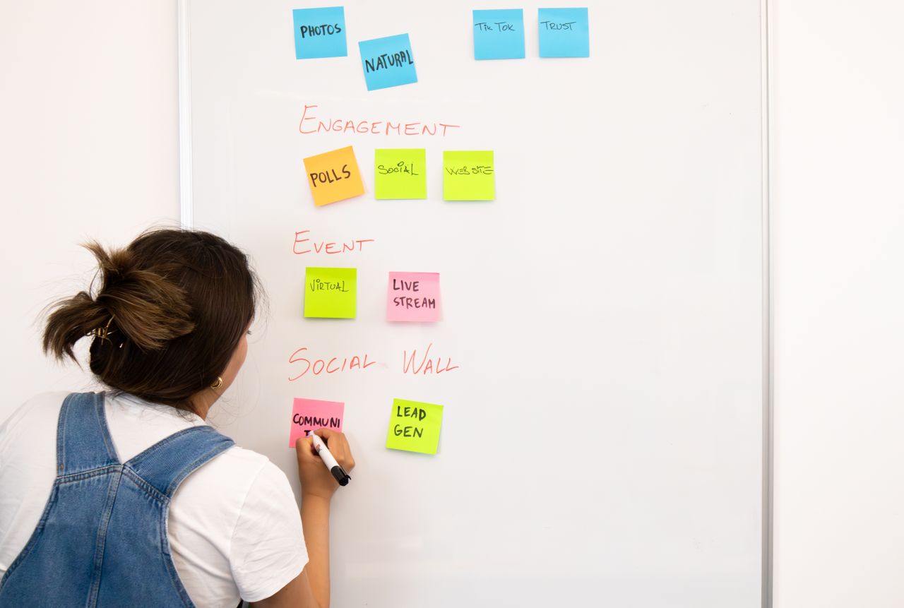 services-01 A woman arranging notes on a whiteboard with colorful sticky notes in an office setting.